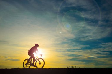 Gün batımında bisiklet süren yakışıklı bir adamın silueti, spor adamı konsepti, işaret fişeği etkisi.