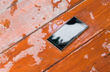 Islak ahşap arka planda su damlaları olan cep telefonu