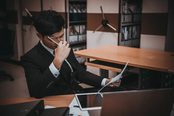 Asian businessman in black suit think idea for work at office,he work overtime alone in a company,dark tone,thailand people