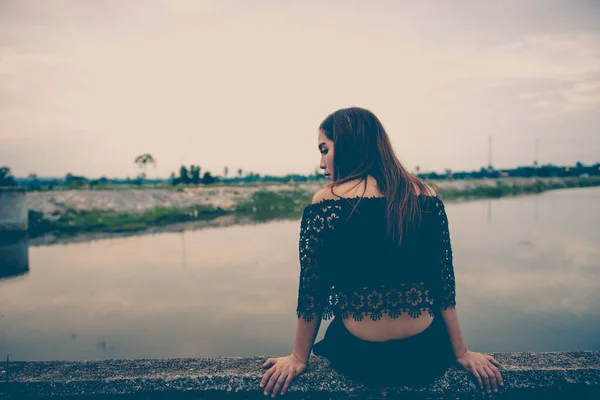 Young pretty girl was sad to sit on the concrete dam, she was disappointed by the sweet love from a lover of her,from back angle,alone heartbreak concept