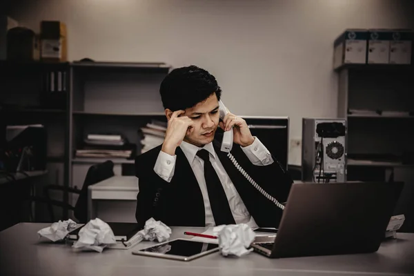 Businessman stress from hard work on the desk at office dark tone.take with boss on telephone,thailand people