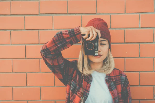彼女はレンガの壁の背景に手でカメラを持つ肖像アジアのヒップスターの女の子 彼女はオレンジのサングラスと赤の帽子のヴィンテージダークスタイルを身に着けています ファッションコンセプト — ストック写真