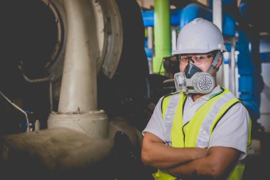 Kazan dairesinde çalışan gözlüklü Asyalı mühendis, ısıtma sistemi ekipmanlarının teknik verilerini kontrol ediyor, Taylandlılar gaz maskesi takıyor.