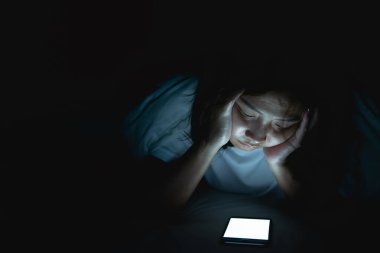 Asyalı kadın gece yatakta akıllı telefonla oyun oynuyor, Taylandlılar, sosyal medya bağımlısı.