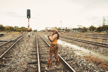 Hipster Asyalı kız fotoğraf çektirmek için poz veriyor, demiryolunda güzel bir kadın tasvir ediyor, modern ergen thai kızının yaşam tarzı, renkli elbiseler, Taylandlı insanlar, orta parmak.