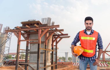 İnşaat mühendisi büyük bir köprüde miğfer tutuyor. İnşaat arka planında.