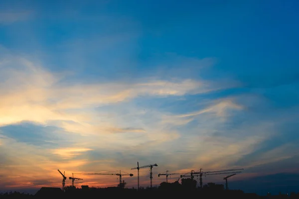 silhouette of a building under construction and the construction cranes in the background of orange sunset