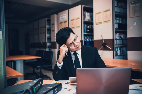 Asian businessman in black suit think idea for work at office,he work overtime alone in a company,dark tone,thailand people