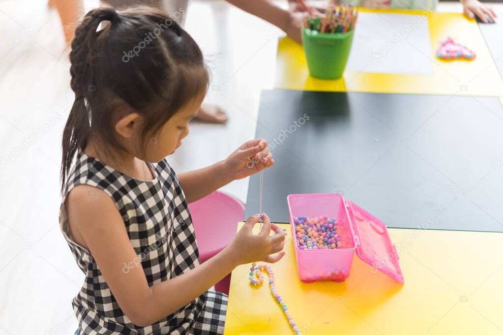 Cute little girl threading beads and making bracelet