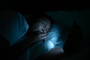 Asyalı kadın gece yatakta akıllı telefonla oyun oynuyor, Taylandlılar, sosyal medya bağımlısı.