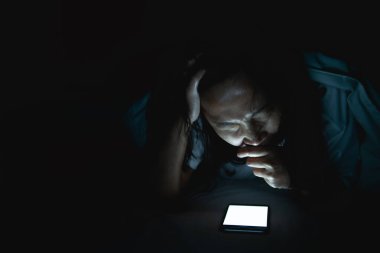 Asyalı kadın gece yatakta akıllı telefonla oyun oynuyor, Taylandlılar, sosyal medya bağımlısı.