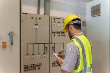 Asyalı elektrik mühendisi kontrol odasındaki elektrik sistemini kontrol etmek ve izlemek için pano tutuyor.