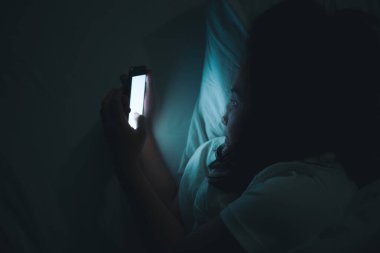 Asyalı kadın gece yatakta akıllı telefonla oyun oynuyor, Taylandlılar, sosyal medya bağımlısı.