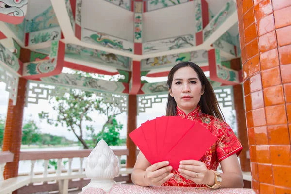happy Chinese new year. Asian woman wearing traditional Cheongsam clothes with red envelopes in hand at Chinese style pavilion