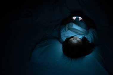 Asyalı kadın gece yatakta akıllı telefonla oyun oynuyor, Taylandlılar, sosyal medya bağımlısı.
