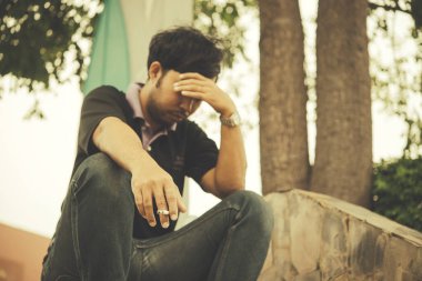 Asyalı bir adam aşktan üzgün, sigara içiyor, otur ve kafaya dokun.