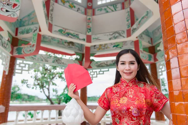happy Chinese new year. Asian woman wearing traditional Cheongsam clothes with red envelopes in hand at Chinese style pavilion