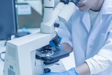 Genç Asyalı bilim adamı bir laboratuarda mikroskoptan bakıyor. Taylandlılar biraz araştırma yapıyor..