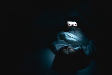 Asyalı kadın gece yatakta akıllı telefonla oyun oynuyor, Taylandlılar, sosyal medya bağımlısı.