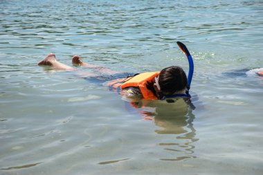 Asyalı turistler deniz kenarında şnorkelle yüzme pratiği yapıyorlar. 