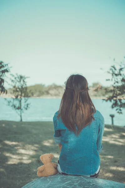 美丽的亚洲女人穿着牛仔裤 泰迪熊在公园的老式风格 伤心的女人的概念 — 图库照片