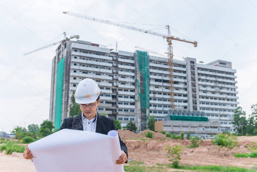 Young asian engineer looking paper plan of the building,blueprint in hand at construction site