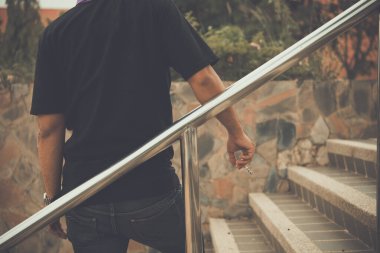 Asyalı yakışıklı adam merdivenlerde arkadan sigara içiyor.