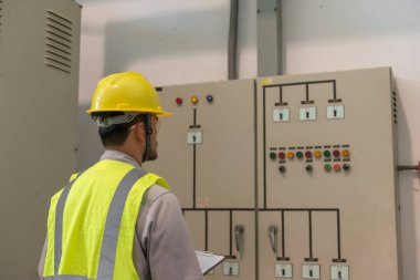 Asyalı elektrik mühendisi kontrol odasındaki elektrik sistemini kontrol etmek ve izlemek için pano tutuyor.