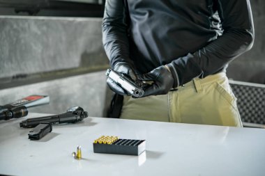 Elinde silahla siyah deri eldivenler giyen Asyalı bir erkek silaha kurşun dolduruyor.