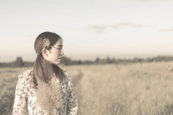 Portait of young beautiful woman with flowers on ear in the fields sepia tone,vintage style,dark,lifestyle