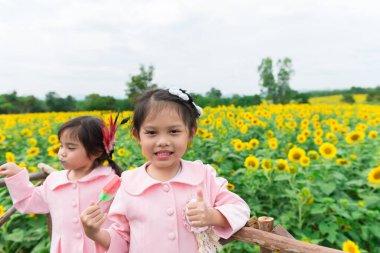 Güneşli bir günde iki çocuk ayçiçeği tarlasında dondurma yiyor.