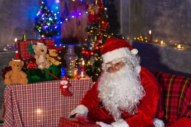 Noel baba holding hediye evde kutusunda, gönderilen hediye kutusu plan vermek çocuklar için sandalye düşünmek oturmak