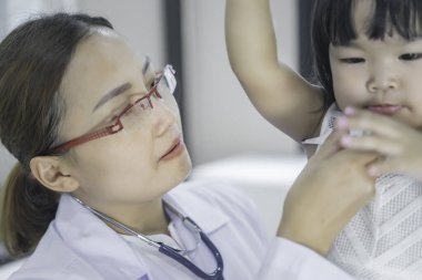 Solunumunu ve kalbini kontrol etmek için steteskop kullanan Asyalı bir doktor, Taylandlı çocukların sağlığını kontrol ediyor.