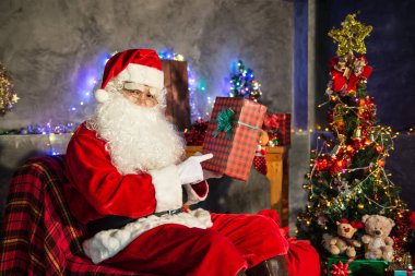 Noel baba holding hediye evde kutusunda, gönderilen hediye kutusu plan vermek çocuklar için sandalye düşünmek oturmak