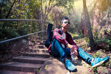 Asyalı yakışıklı adam dağa tırmanmadan önce kayaya oturur.