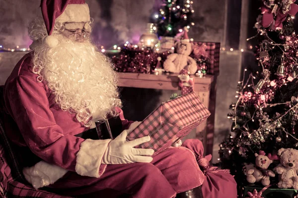 圣诞老人在家里拿着礼品盒 坐在椅子上想着给孩子送礼物盒的计划 — 图库照片