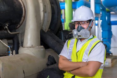Kazan dairesinde çalışan gözlüklü Asyalı mühendis, ısıtma sistemi ekipmanlarının teknik verilerini kontrol ediyor, Taylandlılar gaz maskesi takıyor.