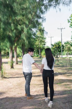 Asyalı yakışıklı adam birlikte yürümek için kadının elini tutuyor.