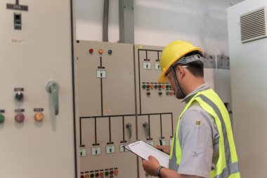 Asyalı elektrik mühendisi kontrol odasındaki elektrik sistemini kontrol etmek ve izlemek için pano tutuyor.