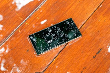 Islak ahşap arka planda su damlaları olan cep telefonu