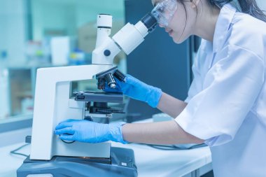 Genç Asyalı bilim adamı bir laboratuarda mikroskoptan bakıyor. Taylandlılar biraz araştırma yapıyor..