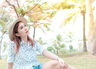 Parlak güneş ışığıyla çimenlerde oturan güzel Asyalı kadın aşkı düşünüyor.