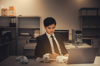 Takım elbiseli Asyalı yakışıklı iş adamı ofiste kağıt parçalarıyla sıkı çalışıyor, genç adam şirketin satışlarının azalması ve karanlık tonda olması konusunda vurgu yapıyor.