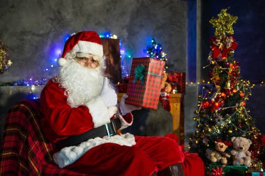 Noel baba holding hediye evde kutusunda, gönderilen hediye kutusu plan vermek çocuklar için sandalye düşünmek oturmak