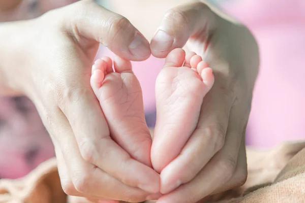 Closeup feet of baby shape heart from hand mom