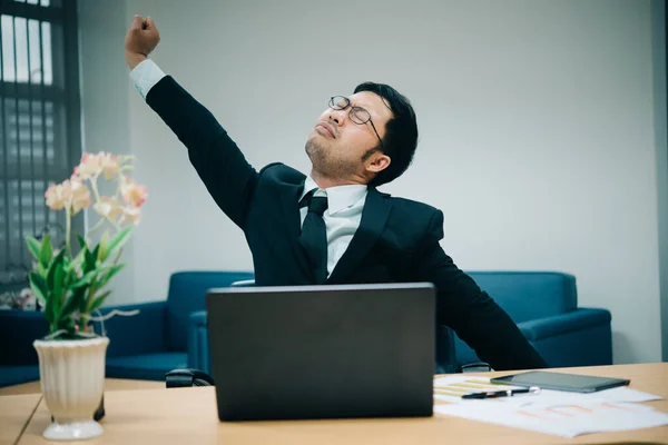 Asian officer man stretching body at the desk of office from back angle,Thailand people,Businessman tired from hard work