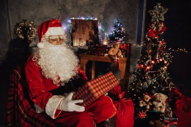 Noel baba holding hediye evde kutusunda, gönderilen hediye kutusu plan vermek çocuklar için sandalye düşünmek oturmak
