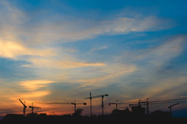 silhouette of a building under construction and the construction cranes in the background of orange sunset