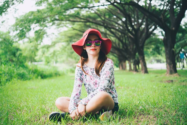 Beautiful asian woman wear red hat and wear pink glasses sit on lawn