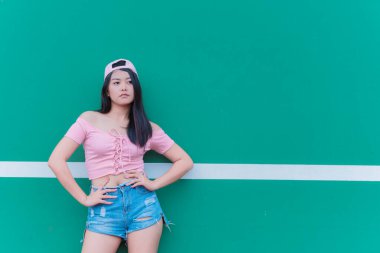 Güzel Asyalı şık bir kızın portresi siyah bir elbise giyer. Duvarda fotoğraf çeker. Tayland gençlerinin yaşam tarzı, modern kadın mutlu konsepti.